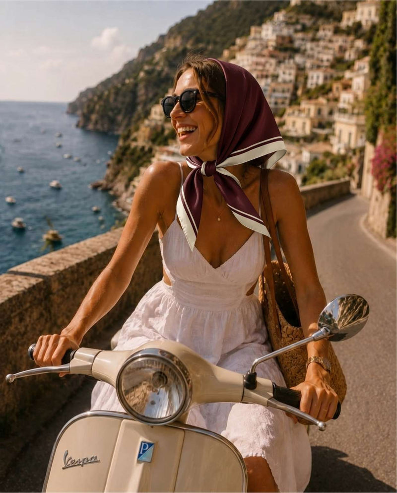 Kvinna på moped i Italien klädd i vit sommarklänning och vinröd sidensjal.